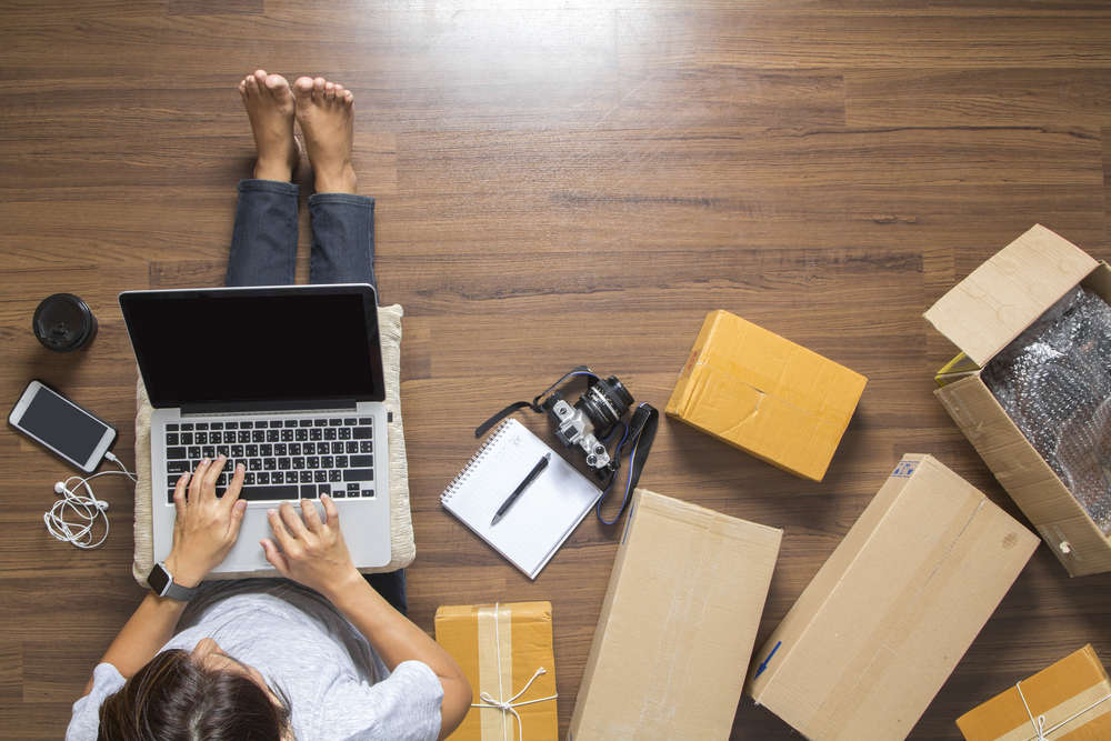 person sitting on the floor on their laptop with boxes that were delivered with international freight servicesthem